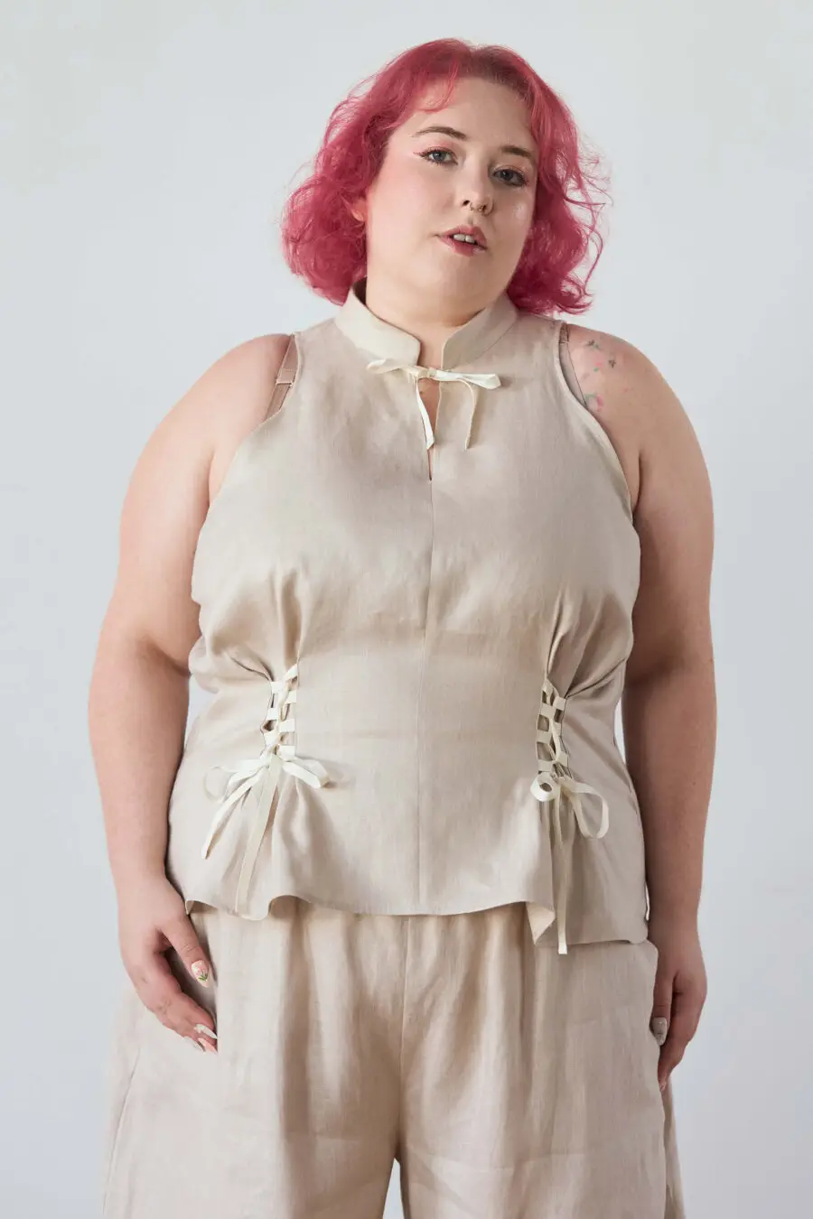 Yvonne sleeveless corset shirt in beige - A sleeveless halter-style shirt made from pink gingham with a structured silhouette and corset-inspired lacing at the waist.