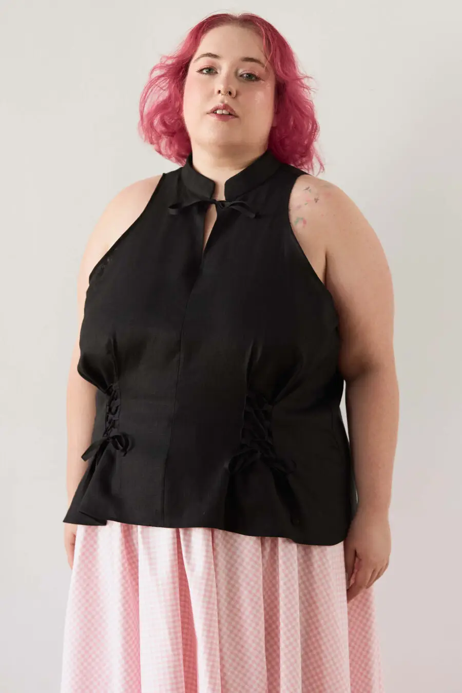 Yvonne sleeveless corset shirt in black - A sleeveless halter-style shirt made from pink gingham with a structured silhouette and corset-inspired lacing at the waist.