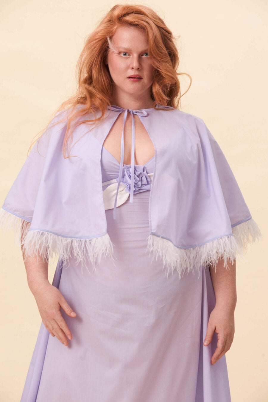 Birds of a Feather cape in lavender voille - Cut in a short, flared silhouette that rests lightly on the shoulders. The cape ties at the neck, creating a clean opening through the front. Along the edge, a feather trim introduces texture and subtle motion. Balanced between structure and softness.