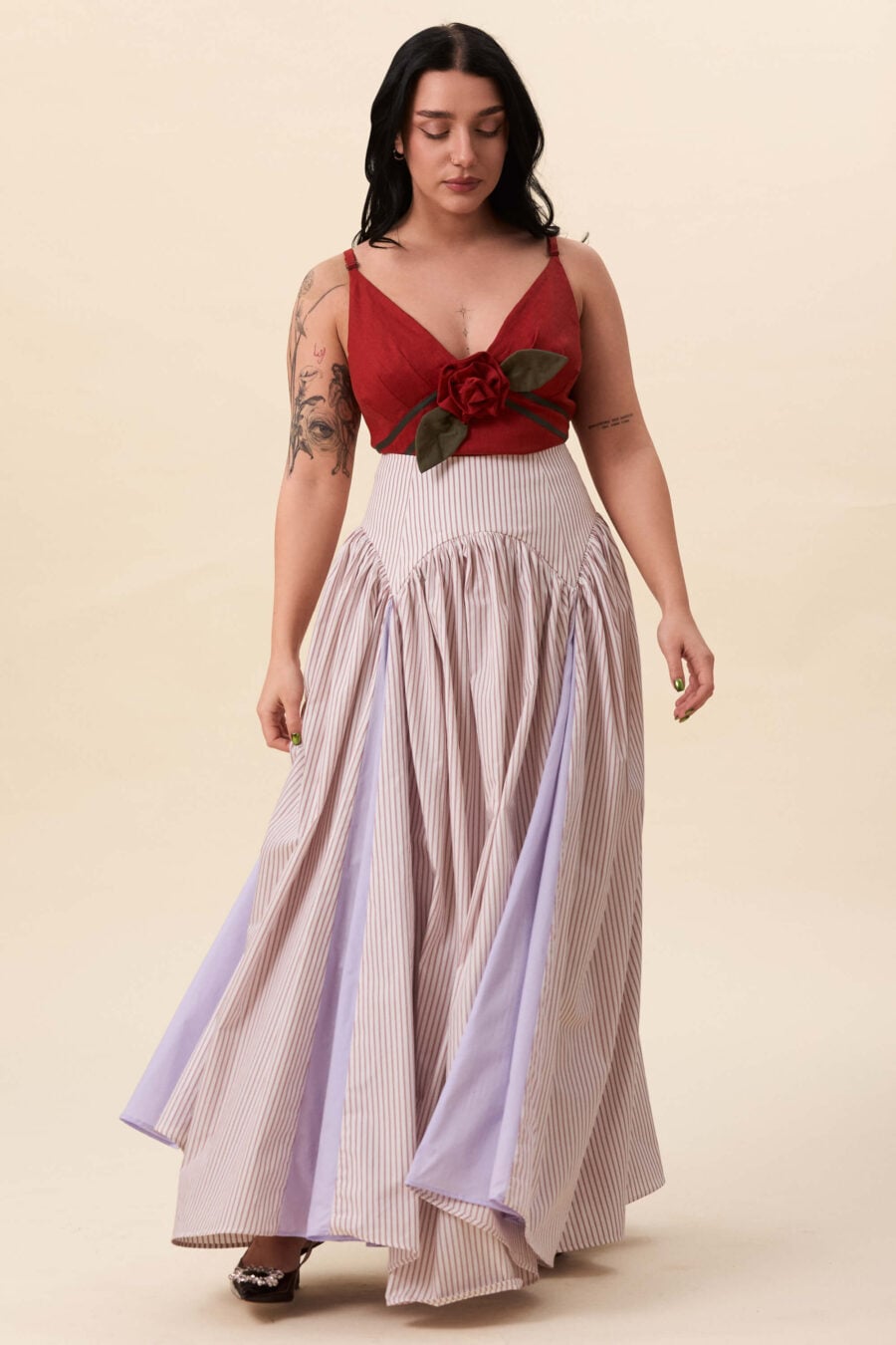 Cordelia Gray maxi skirt in red stripes  The waist holds a fitted structure before releasing into a full, gathered skirt. Contrasting panels at the front and back shape the silhouette, introducing variation and rhythm as the garment moves.
