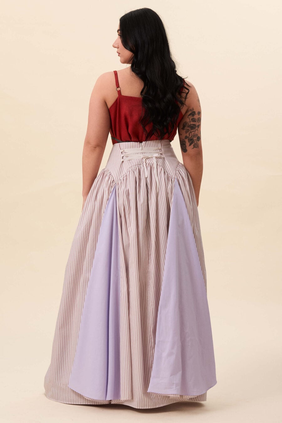 Cordelia Gray maxi skirt in red stripes - The waist holds a fitted structure before releasing into a full, gathered skirt. Contrasting panels at the front and back shape the silhouette, introducing variation and rhythm as the garment moves.