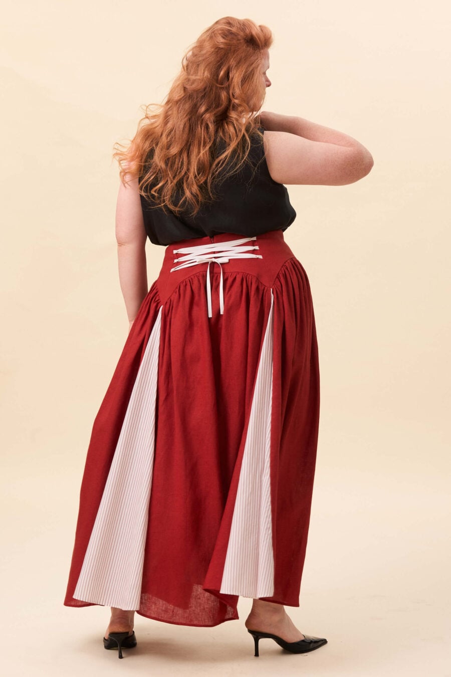 Cordelia Gray maxi skirt in tomato red - The waist holds a fitted structure before releasing into a full, gathered skirt. Contrasting panels at the front and back shape the silhouette, introducing variation and rhythm as the garment moves.