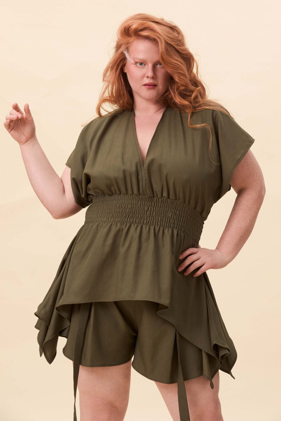 Nemesis ruched top in olive green - A structured top defined by a deep V neckline and a shaped waist panel. The bodice is fitted through a smocked section, creating tension and adaptability. From the waist, the fabric releases into soft, pointed extensions that move away from the body.
