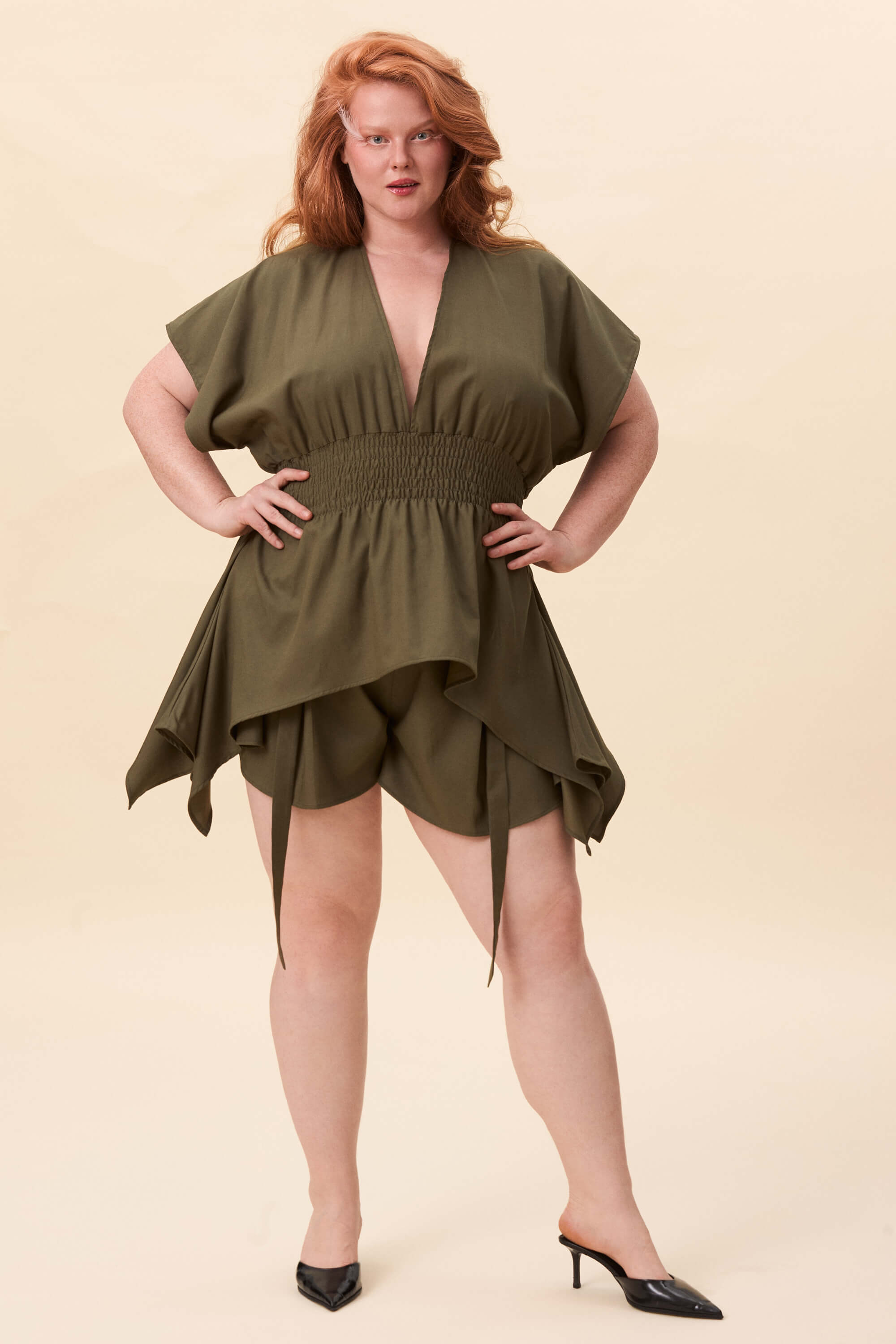 Spring 2026 Nemesis Ruched Top In Olive Green 2 Nemesis Ruched Top In Olive Green Nemesis ruched top in olive green A structured top defined by a deep V neckline and a shaped waist panel. The bodice is fitted through a smocked section, creating tension and adaptability. From the waist, the fabric releases into soft, pointed extensions that move away from the body.