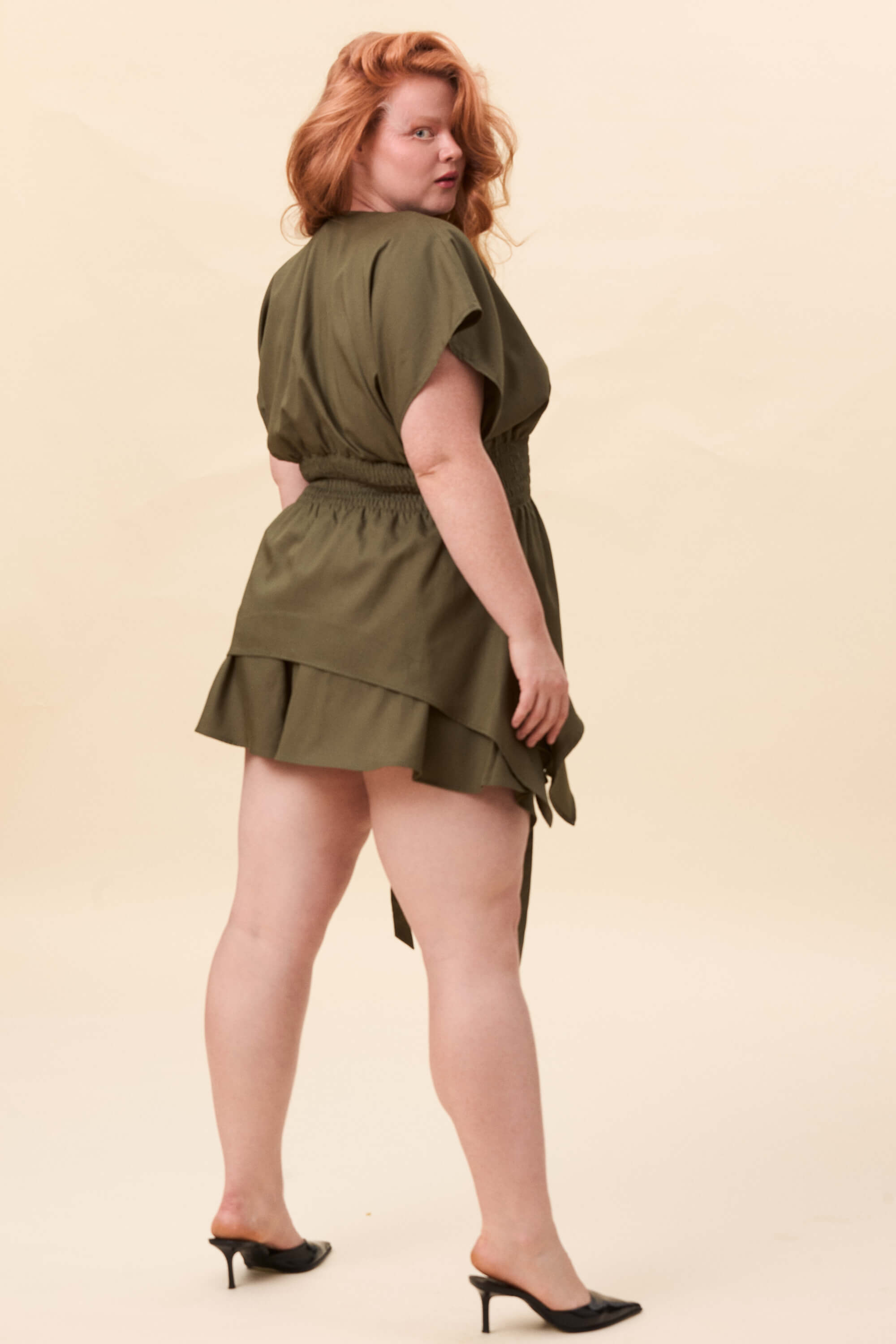 Spring 2026 Nemesis Ruched Top In Olive Green 6 Nemesis Ruched Top In Olive Green Nemesis ruched top in olive green A structured top defined by a deep V neckline and a shaped waist panel. The bodice is fitted through a smocked section, creating tension and adaptability. From the waist, the fabric releases into soft, pointed extensions that move away from the body.