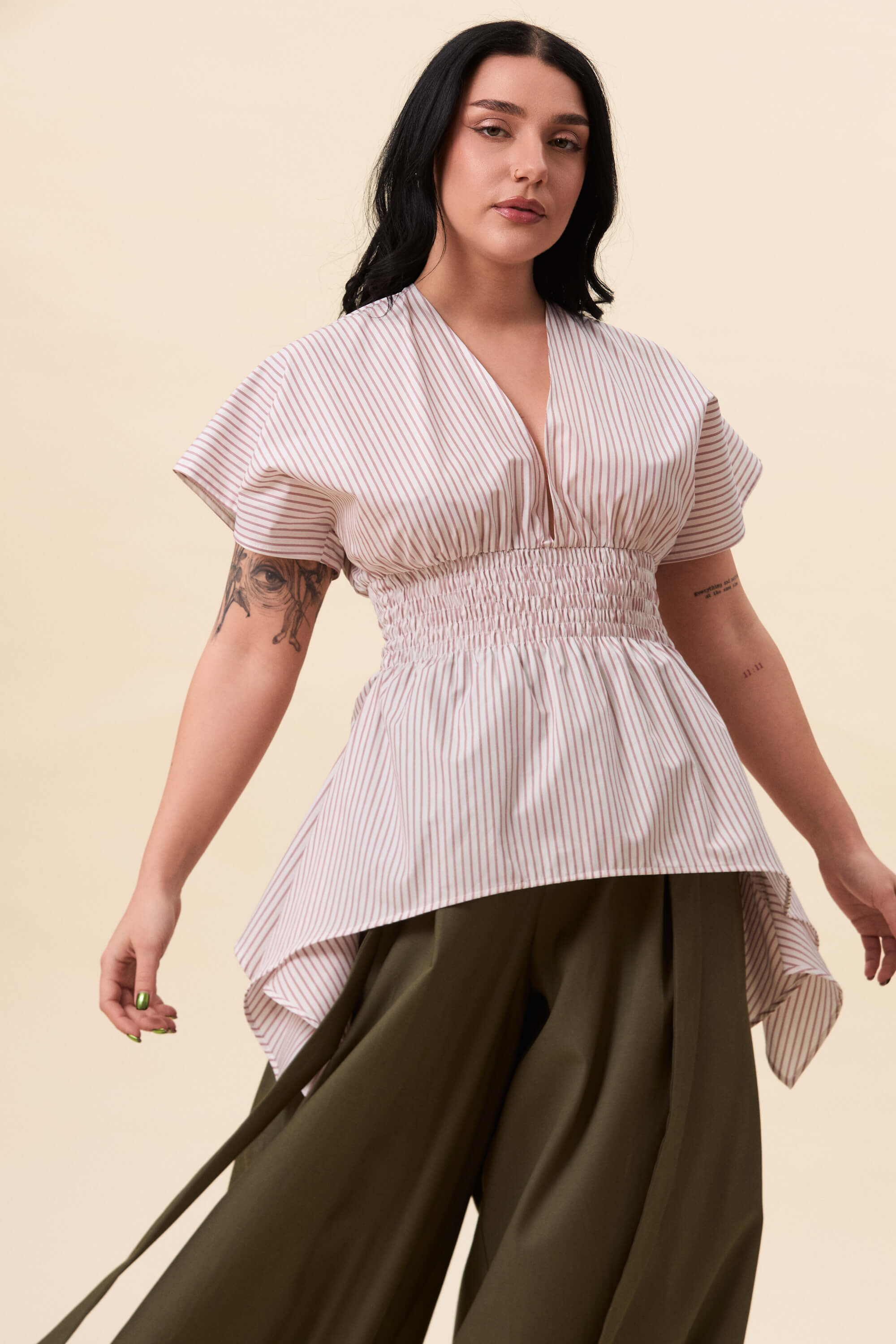 Spring 2026 Nemesis Ruched Top In Red Stripes 2 Nemesis Ruched Top In Red Stripes Nemesis ruched top in red stripes A structured top defined by a deep V neckline and a shaped waist panel. The bodice is fitted through a smocked section, creating tension and adaptability. From the waist, the fabric releases into soft, pointed extensions that move away from the body.