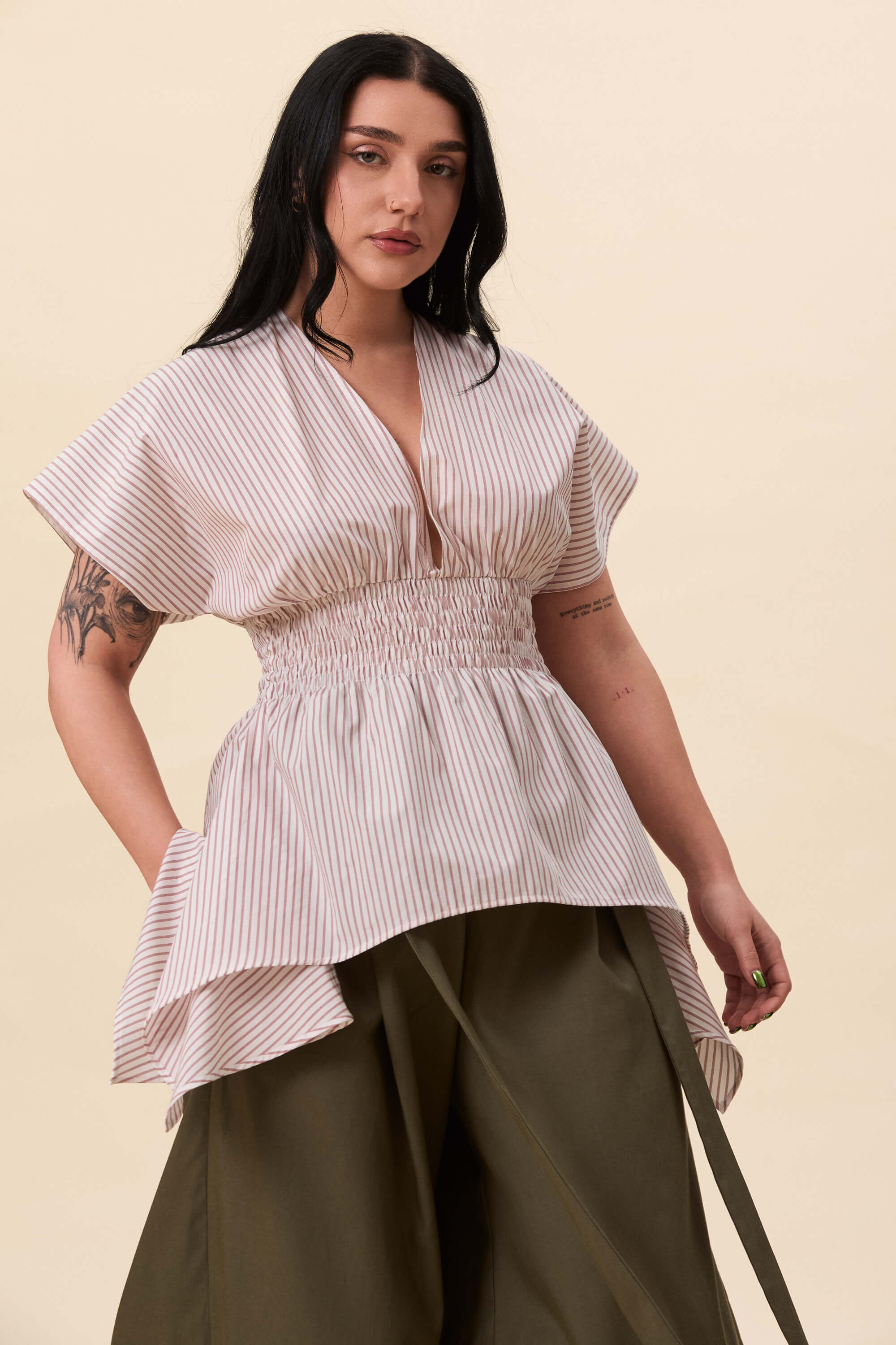 Spring 2026 Nemesis Ruched Top In Red Stripes 4 Nemesis Ruched Top In Red Stripes Nemesis ruched top in red stripes A structured top defined by a deep V neckline and a shaped waist panel. The bodice is fitted through a smocked section, creating tension and adaptability. From the waist, the fabric releases into soft, pointed extensions that move away from the body.