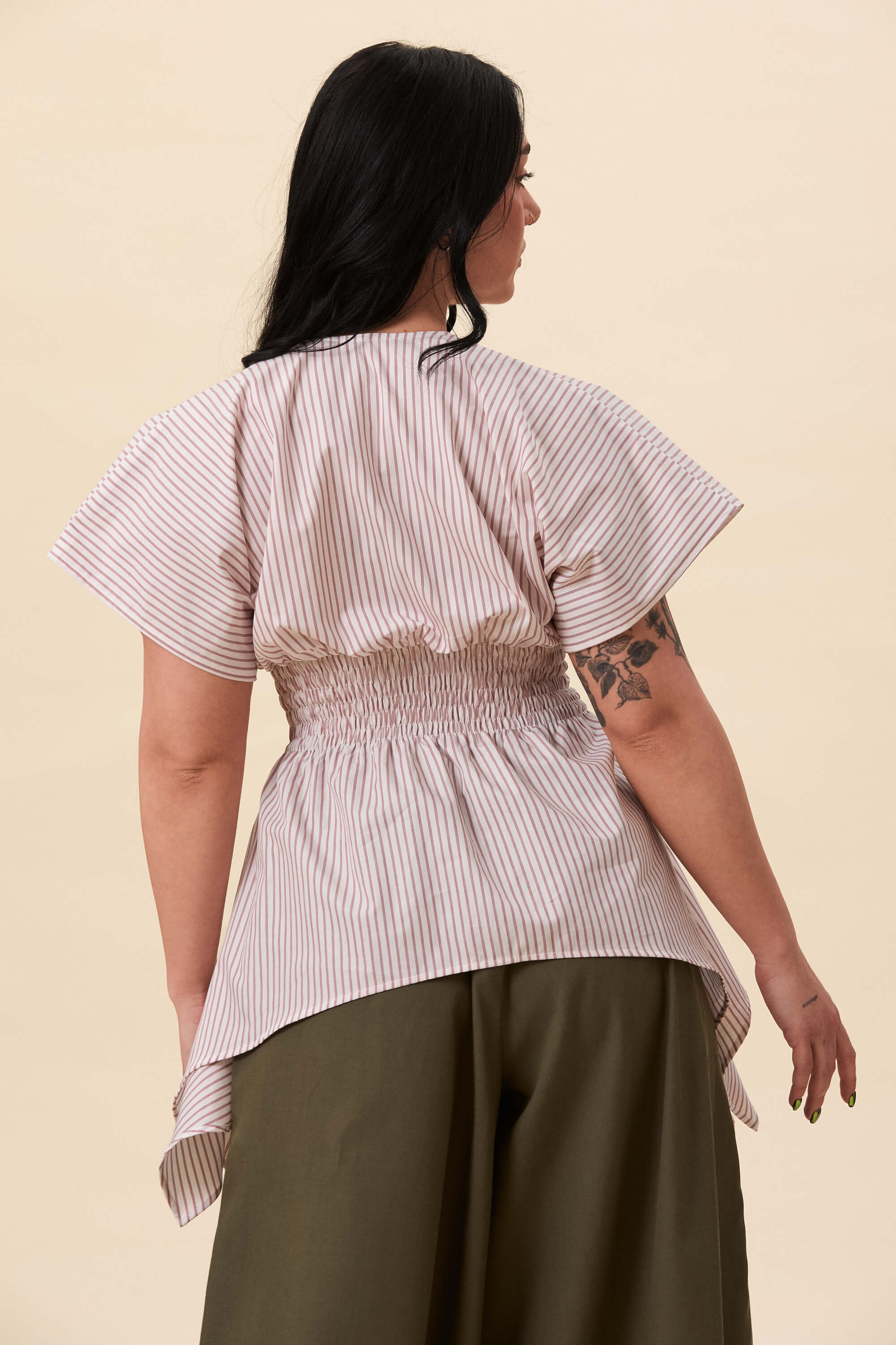 Spring 2026 Nemesis Ruched Top In Red Stripes 5 Nemesis Ruched Top In Red Stripes Nemesis ruched top in red stripes A structured top defined by a deep V neckline and a shaped waist panel. The bodice is fitted through a smocked section, creating tension and adaptability. From the waist, the fabric releases into soft, pointed extensions that move away from the body.