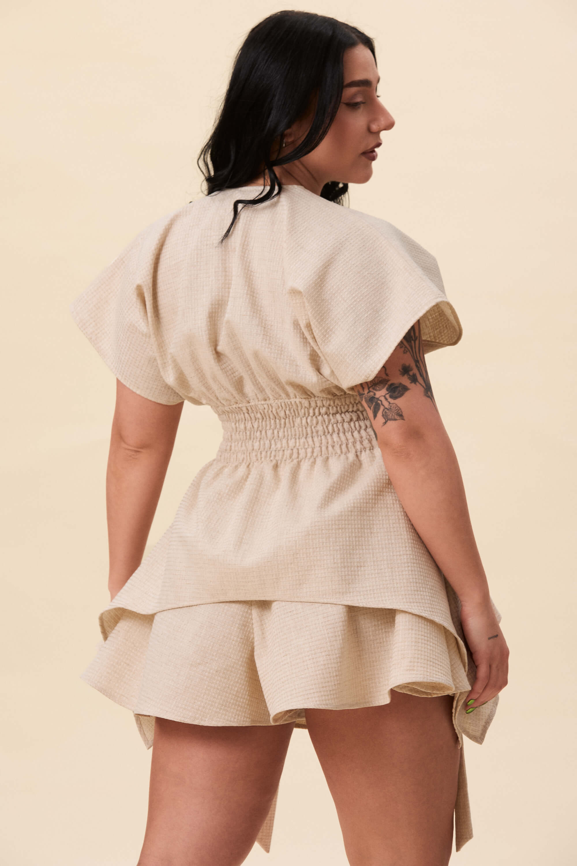 Spring 2026 Nemesis Ruched Top In Textured Beige 5 Nemesis Ruched Top In Textured Beige Nemesis ruched top in textured beige A structured top defined by a deep V neckline and a shaped waist panel. The bodice is fitted through a smocked section, creating tension and adaptability. From the waist, the fabric releases into soft, pointed extensions that move away from the body.