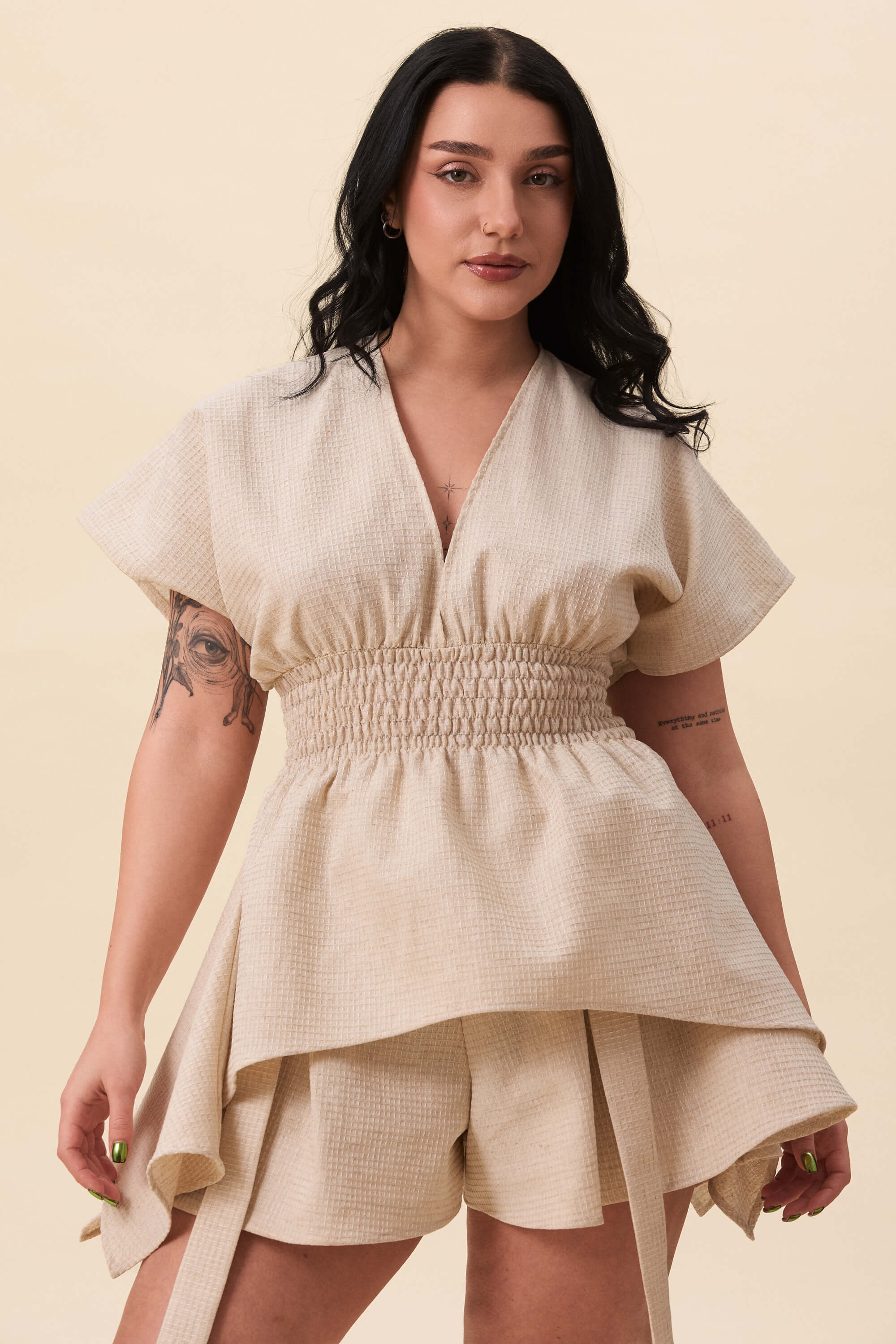 Spring 2026 Nemesis Ruched Top In Textured Beige 6 Nemesis Ruched Top In Textured Beige Nemesis ruched top in textured beige A structured top defined by a deep V neckline and a shaped waist panel. The bodice is fitted through a smocked section, creating tension and adaptability. From the waist, the fabric releases into soft, pointed extensions that move away from the body.