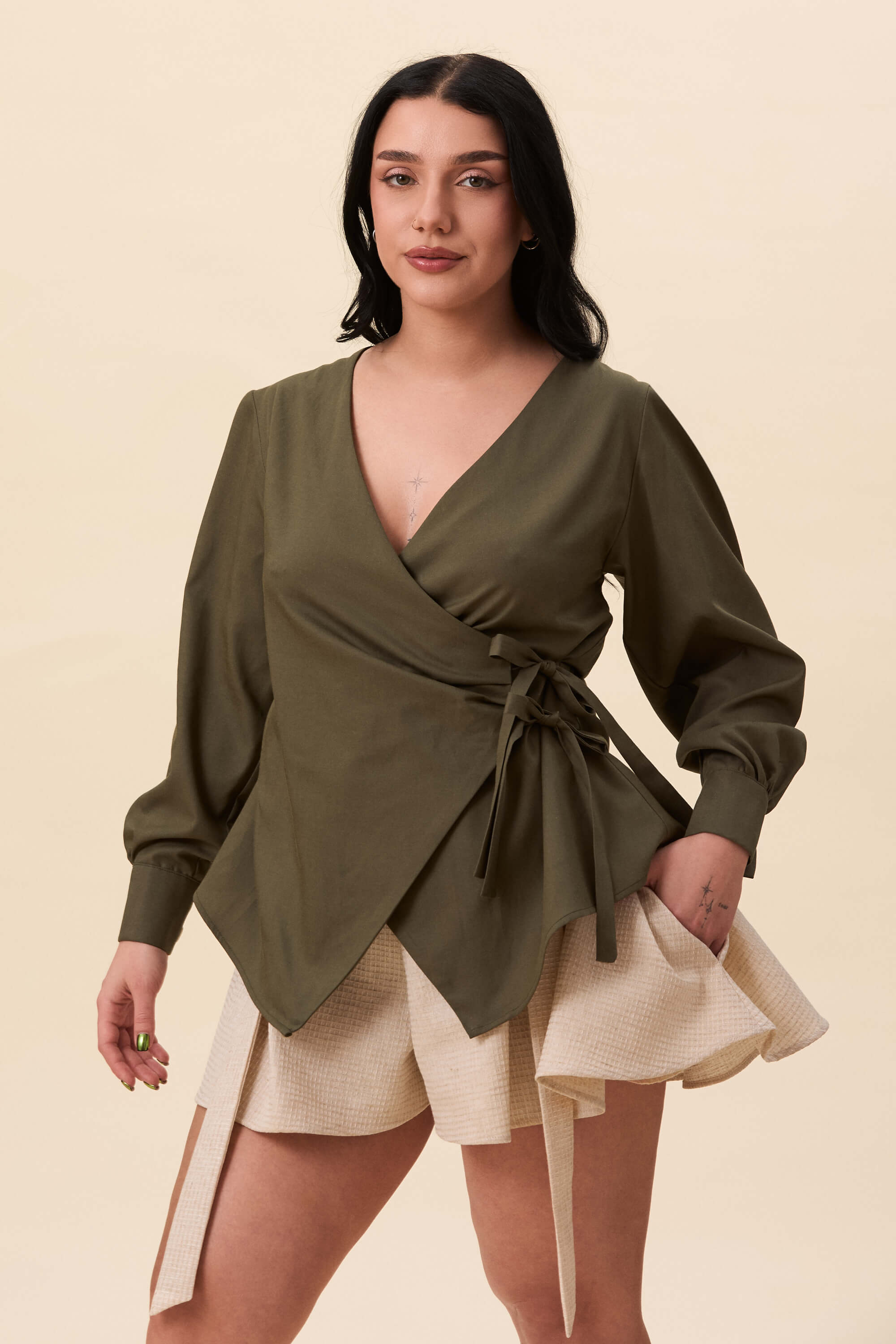Spring 2026 Strong Poison Wrap Shirt In Olive Green 5 Strong Poison Wrap Shirt In Olive Green Strong Poison wrap shirt in olive green A wrap shirt shaped through angled lines rather than volume. The front crosses into a sharp, pointed hem, fastening with slender ties at the side. Sleeves are softly structured, finished with extended cuffs.