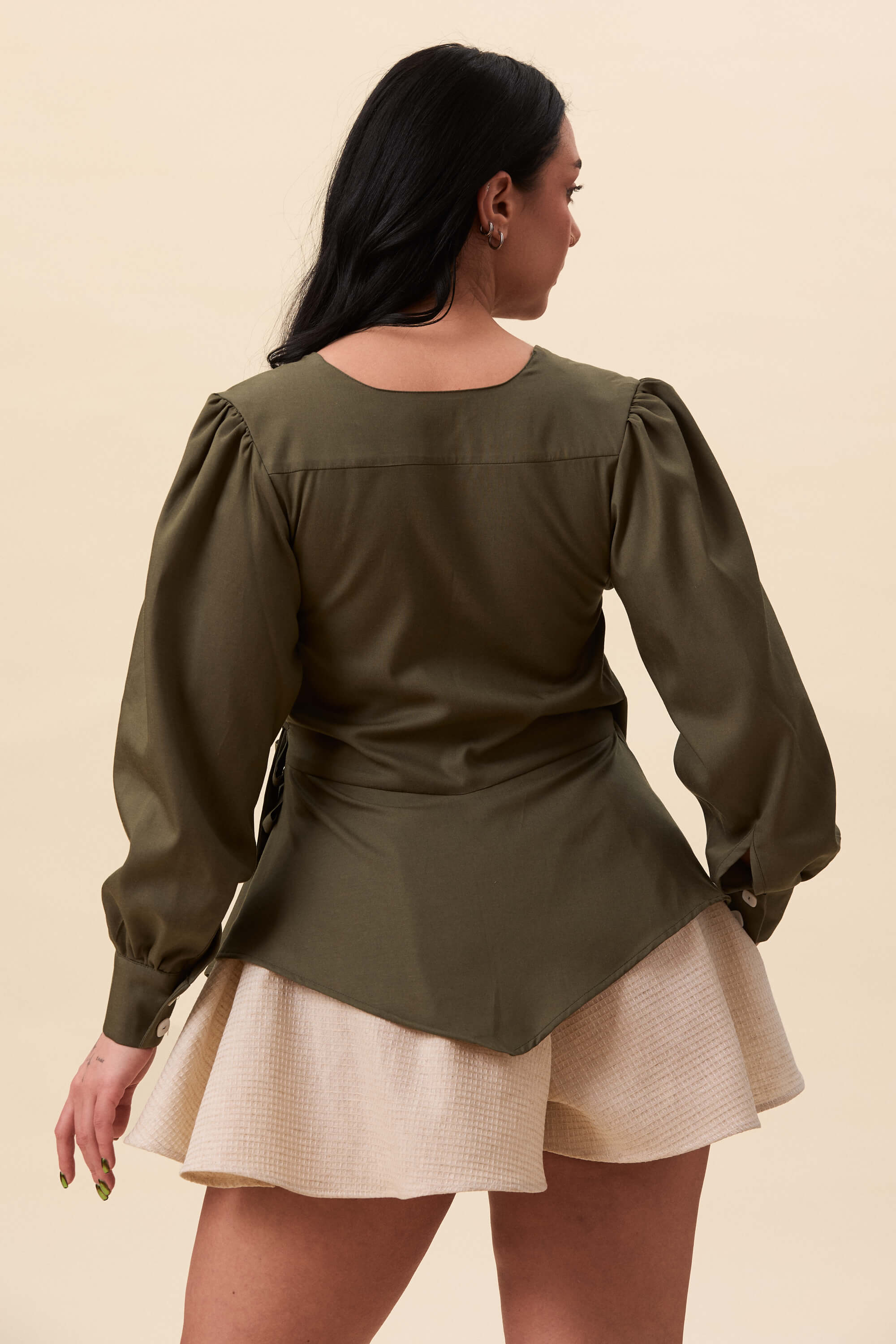 Spring 2026 Strong Poison Wrap Shirt In Olive Green 8 Strong Poison Wrap Shirt In Olive Green Strong Poison wrap shirt in olive green A wrap shirt shaped through angled lines rather than volume. The front crosses into a sharp, pointed hem, fastening with slender ties at the side. Sleeves are softly structured, finished with extended cuffs.