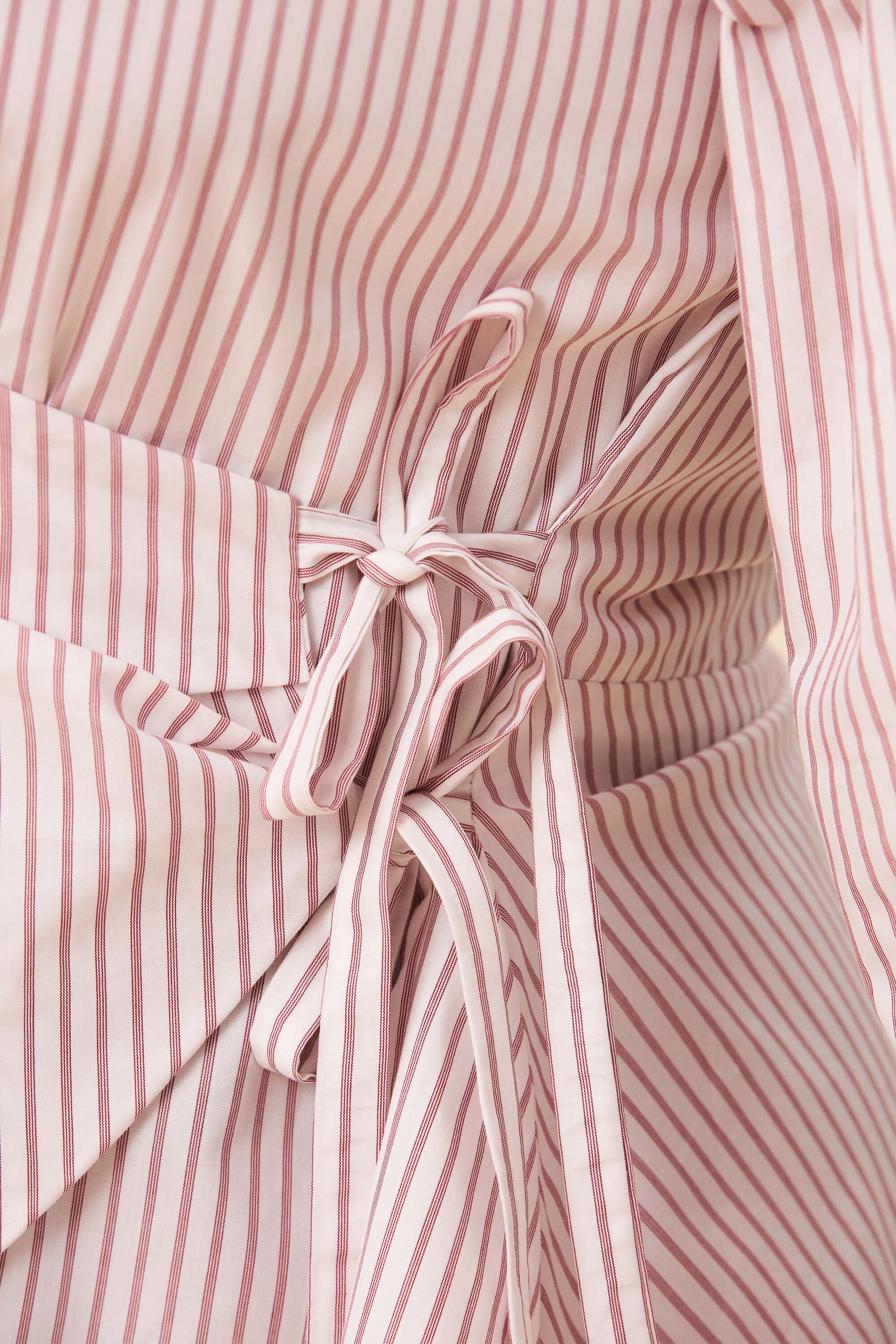 Spring 2026 Strong Poison Wrap Shirt In Red Stripes 4 Strong Poison Wrap Shirt In Red Stripes Strong Poison wrap shirt in red stripes A wrap shirt shaped through angled lines rather than volume. The front crosses into a sharp, pointed hem, fastening with slender ties at the side. Sleeves are softly structured, finished with extended cuffs.