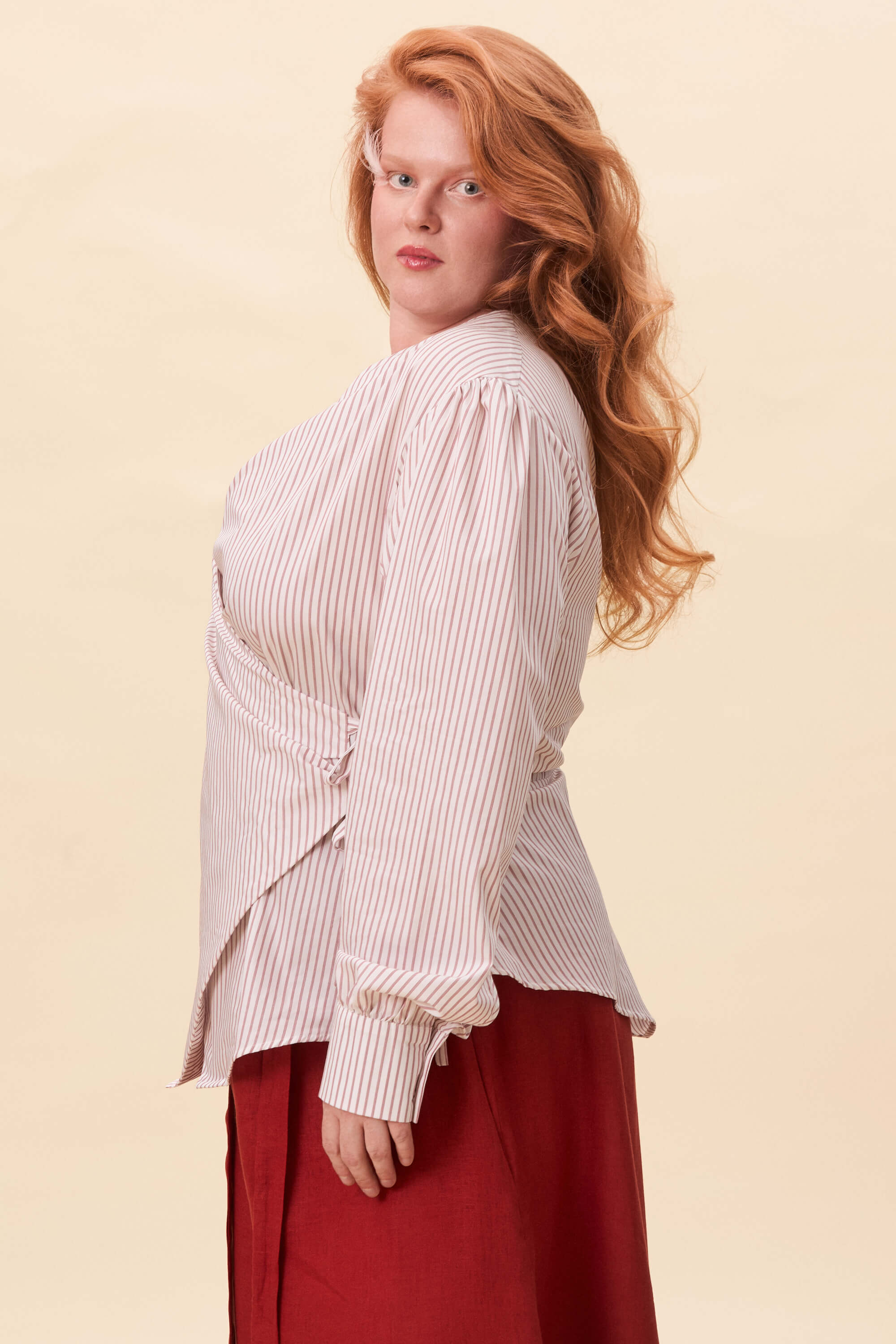 Spring 2026 Strong Poison Wrap Shirt In Red Stripes 5 Strong Poison Wrap Shirt In Red Stripes Strong Poison wrap shirt in red stripes A wrap shirt shaped through angled lines rather than volume. The front crosses into a sharp, pointed hem, fastening with slender ties at the side. Sleeves are softly structured, finished with extended cuffs.